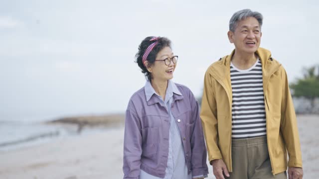 따뜻한 옷으로 멀리 바라보는 해변의 아시아 중국인 노인 부부