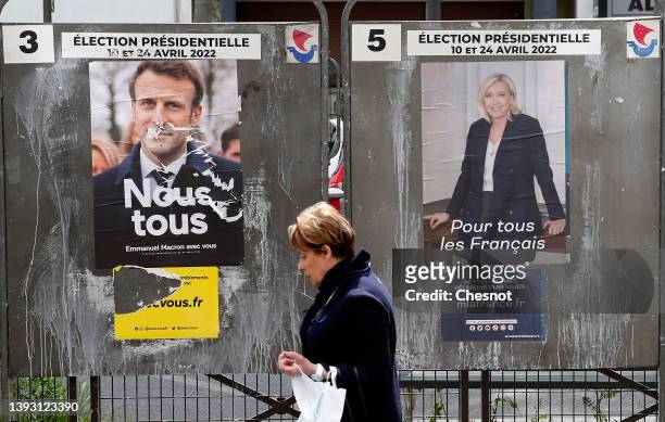 Woman walks past official campaign posters of Marine Le Pen, leader of the far-right Rassemblement national party and French President Emmanuel...