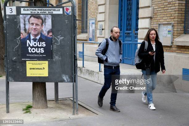 Couple walk past an official campaign poster of French President Emmanuel Macron 'La République en marche' , candidate in the 2022 French...