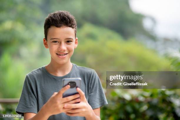 smiling teen boy with a smart phone standing outside - one teenage boy only stock pictures, royalty-free photos & images