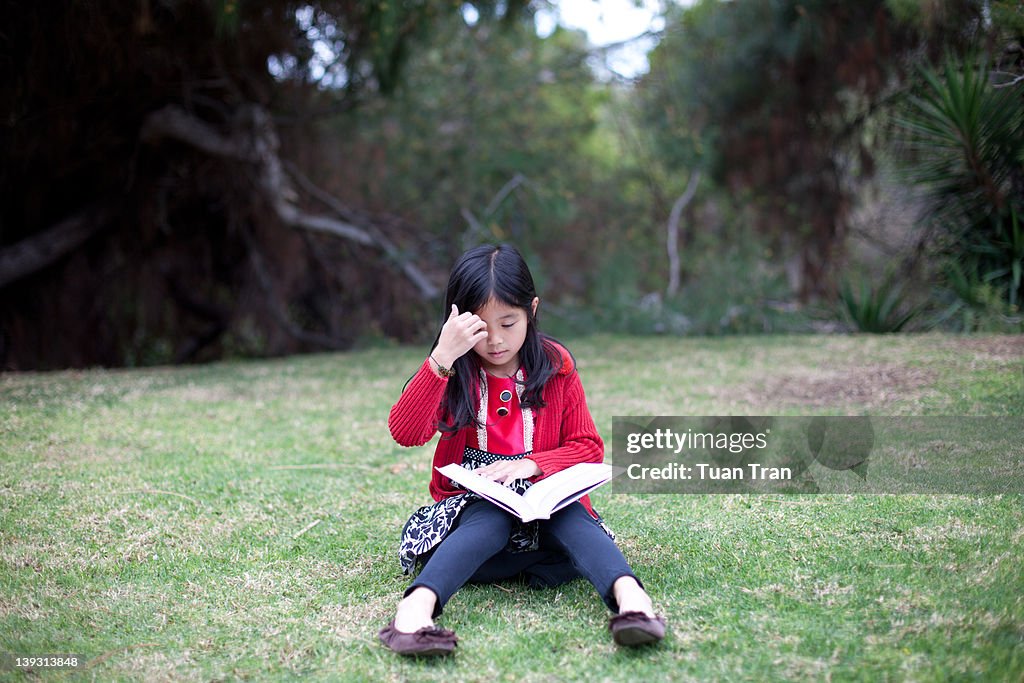 Young Asian girl reading book at park