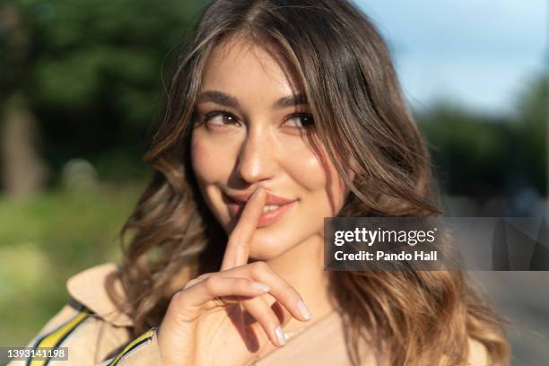 close-up portrait of a young brunette woman smiling, index finger on upper lip - hazel eyes stock pictures, royalty-free photos & images