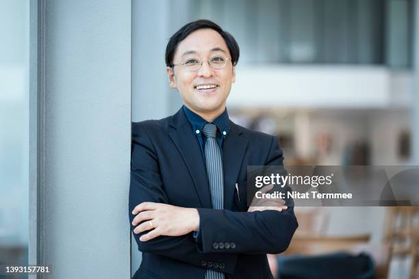 importance of personality development for business entrepreneur. portrait of a japanese business owner in a hotel lobby while standing  with his arms crossed during business travel. he is reliable and leadership. - business owner suit fotografías e imágenes de stock