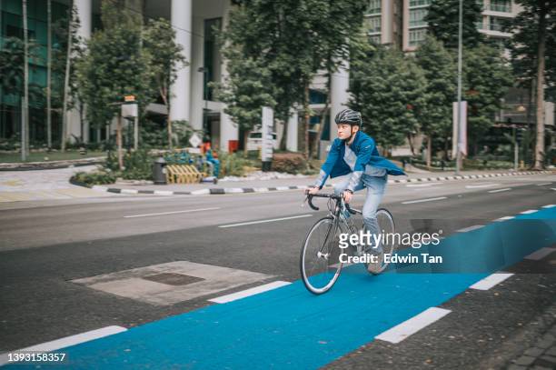 asian chinese man cycling in the city on bicycle lane to work sustainability lifestyle - bike sharing stock pictures, royalty-free photos & images