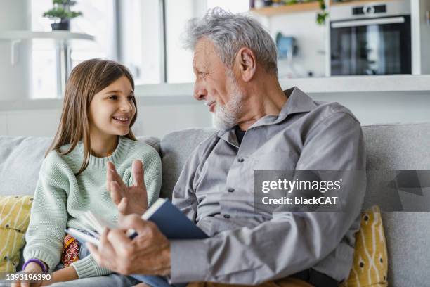 grandfather reading a book to the granddaughter at home - grandfather stockfoto's en -beelden