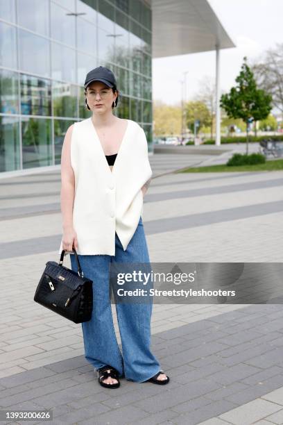 Influencer Maria Barteczko wearing a beige oversized knitted vest by Zara, blue wide leg denim jeans by Zara, a black leather baseball cap by Arket,...