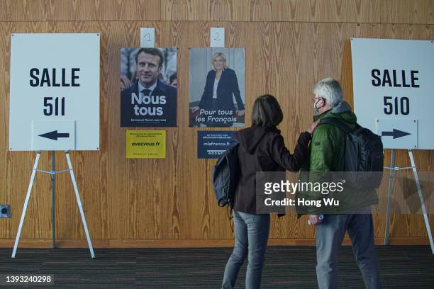 French citizen walk by posters of candidates Emmanuel Macron and Marine Le Pen as they go to vote in the second round of France's presidential...