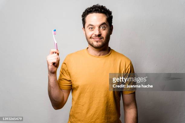 man dressed in yellow t-shirt with surprised expression while holding his toothbrush. - toothbrush ストックフォトと画像