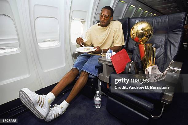 Guard Kobe Bryant of the Los Angeles Lakers eats an in-flight meal with the championship trophy beside him after Game Four of the 2002 NBA Finals...