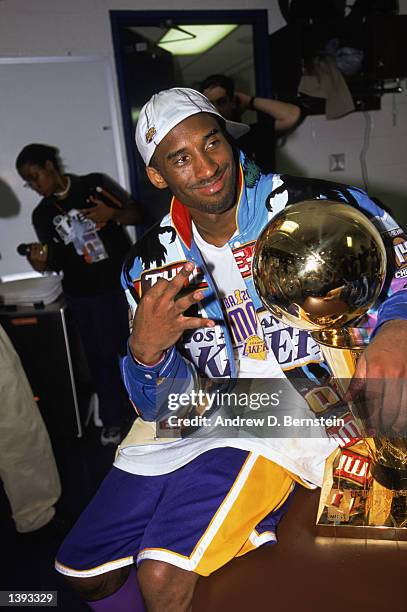 Guard Kobe Bryant of the Los Angeles Lakers sits with the trophy in the locker room as he gestures in reference to winning three championships in a...