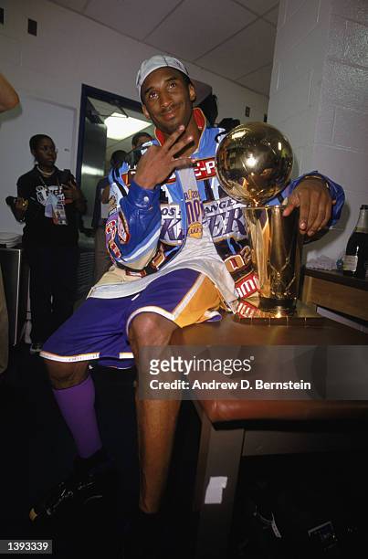 Guard Kobe Bryant of the Los Angeles Lakers sits with the trophy in the locker room as he gestures in reference to winning three championships in a...
