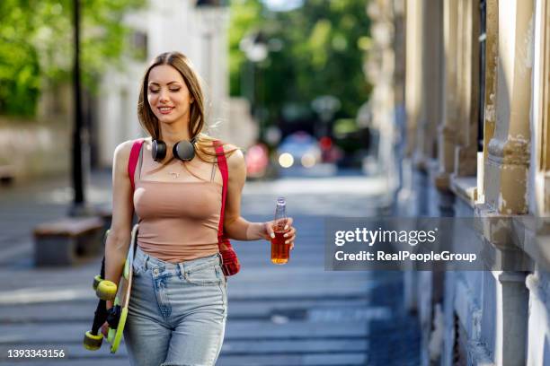 young woman walking with skateboard in hand on city street - subculture stock pictures, royalty-free photos & images