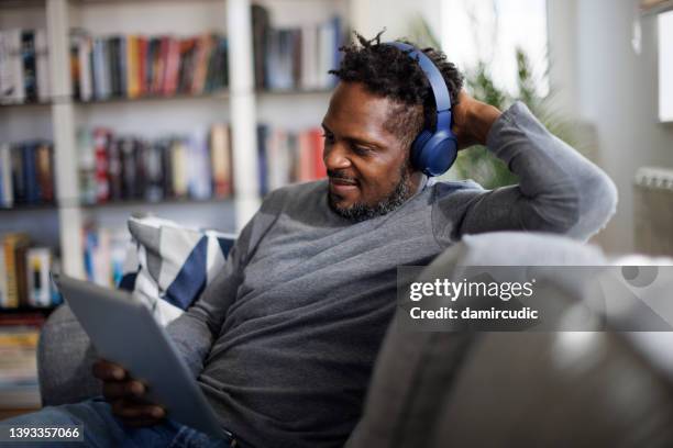 smiling man with bluetooth headphones watching movie on digital tablet at home - tv phone tablet stock pictures, royalty-free photos & images