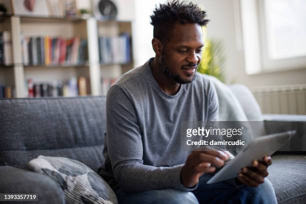 lächelnder junge mann mit digital-tablette zu hause - tv phone tablet stock-fotos und bilder