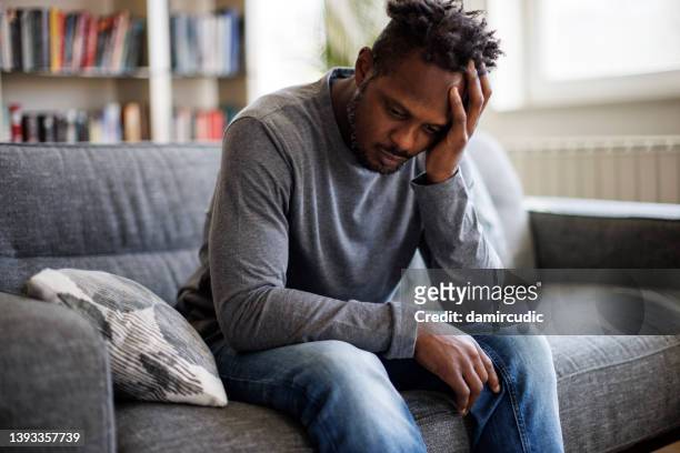 worried man sitting on couch at home - introspection stock pictures, royalty-free photos & images
