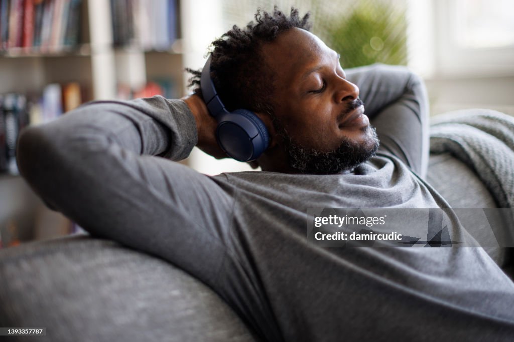 Young man enjoying music over headphones while relaxing on the sofa at home