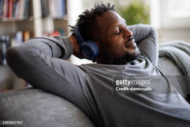 young man enjoying music over headphones while relaxing on the sofa at home - rest stock pictures, royalty-free photos & images