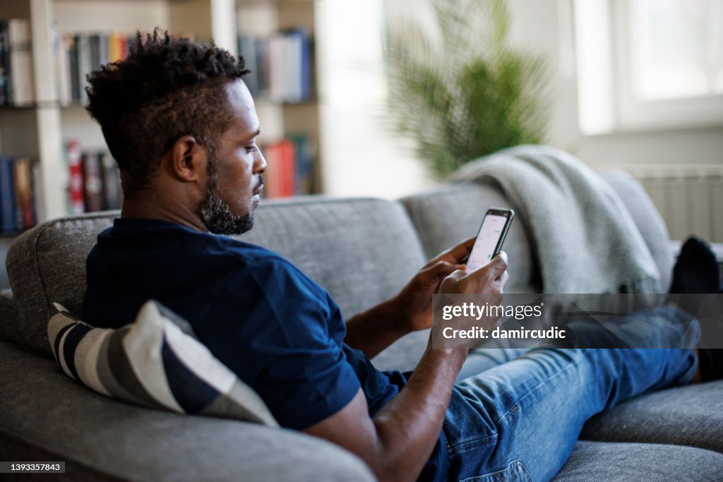 Man sitting on couch and sending text message on phone