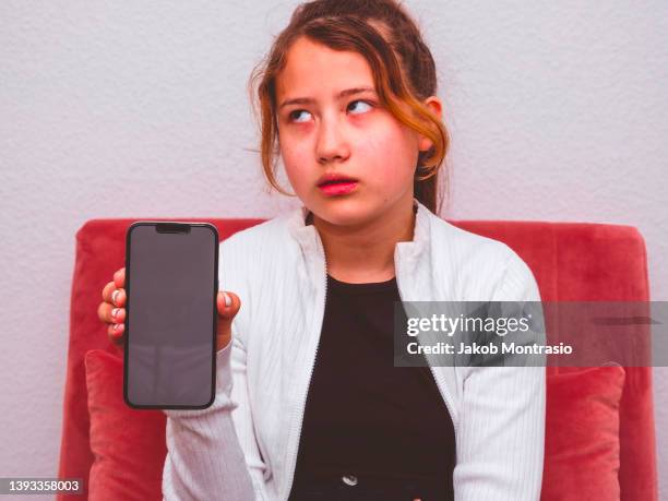 eurasian teenager with a disappointed facial expression presenting an blue iphone 13 pro with a blank placeholder screen - eye roll stock pictures, royalty-free photos & images