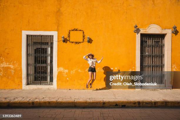 frau springt auf den hintergrund der gelben wand in der stadt izamal in mexiko - merida mexico stock-fotos und bilder