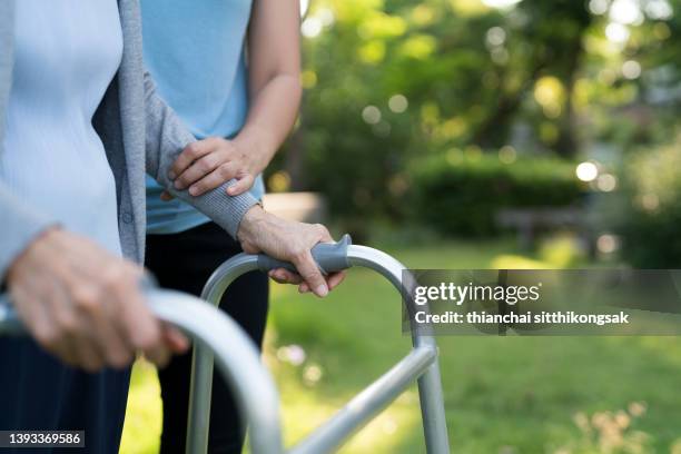 image of an unrecognizable senior woman being assisted to walk using a walker by caregiver at park. - walking frame stock pictures, royalty-free photos & images