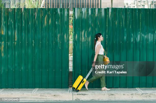 a young southeast asian woman is walking with luggage in the city street - philippines women fotografías e imágenes de stock