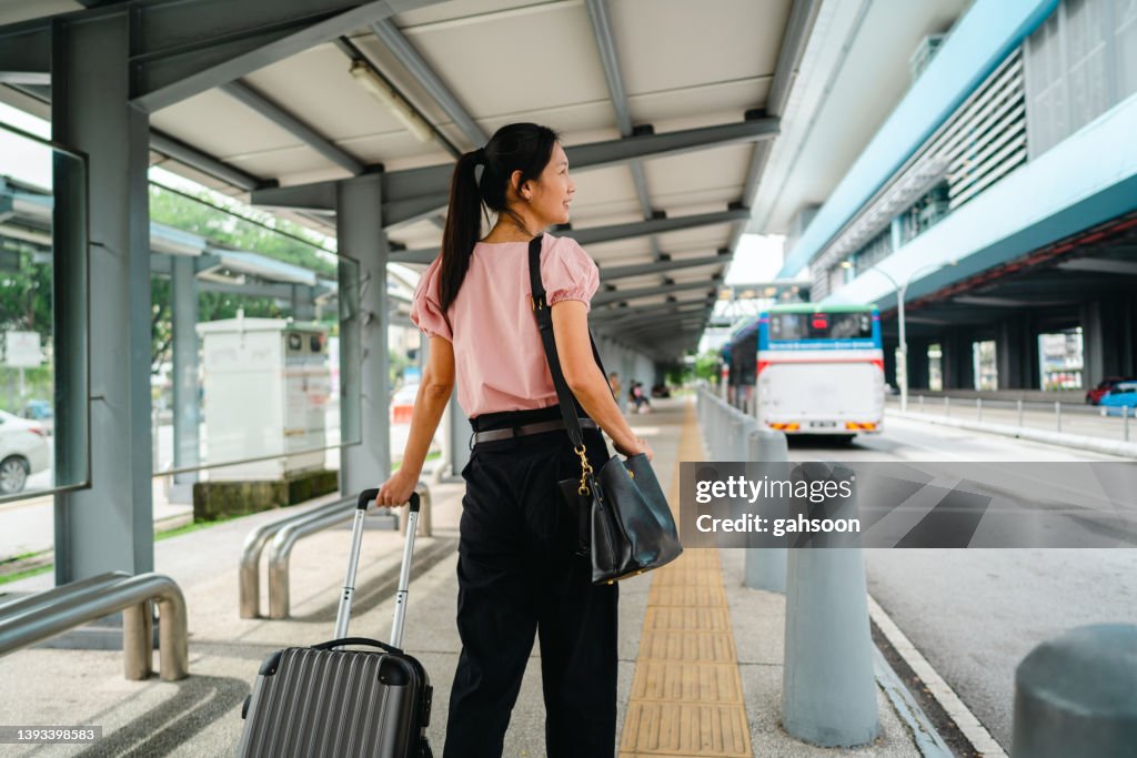 Mujer caminando en la estación con maleta y bolso de cuero.