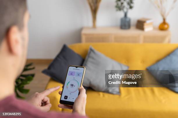 visão sobre o ombro de um homem usando um aplicativo inteligente de controle de temperatura em casa - thermostat - fotografias e filmes do acervo