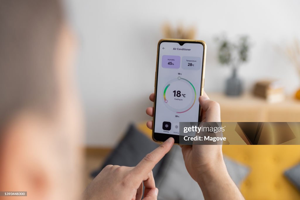 Vista ravvicinata di un uomo che regola il condizionatore d'aria di casa con un'app per smartphone.