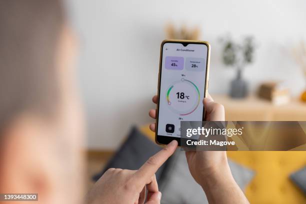 close-up view of a man adjusting his home air conditioner with a smart phone app. - mobile devices at home stock pictures, royalty-free photos & images