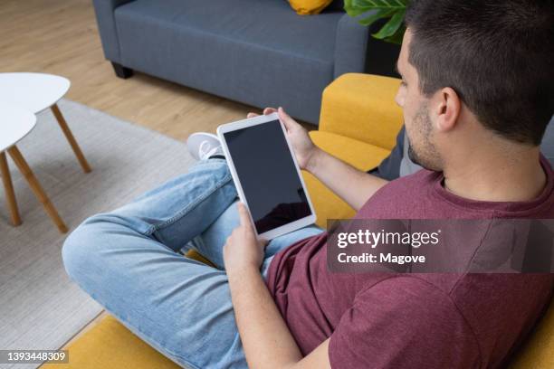 a man sitting on the sofa at home looking at his digital tablet - back of sofa stock pictures, royalty-free photos & images