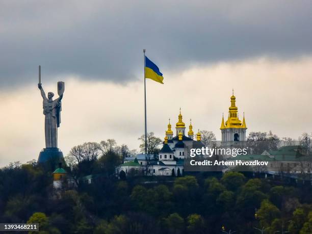 motherland monument stands by the kyiv pechersk lavra monastery and tall flagpole with ukrainian national flag - kiew stock-fotos und bilder