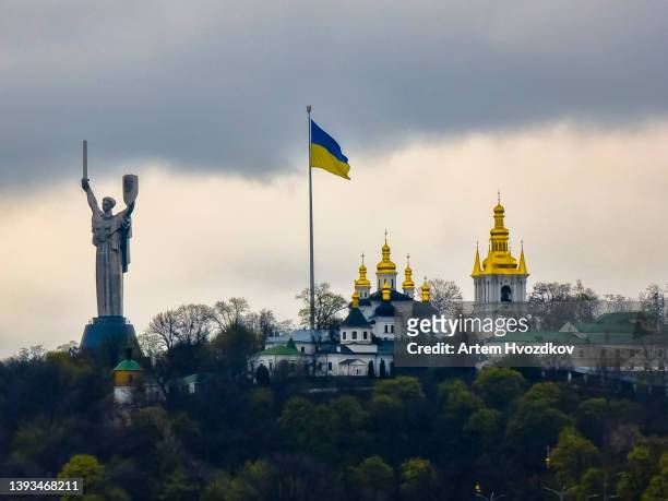 motherland monument stands by the kyiv pechersk lavra monastery and tall flagpole with ukrainian national flag - kiev photos et images de collection