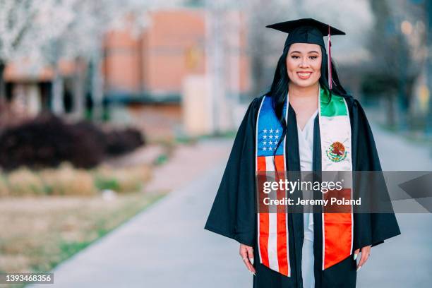 close-up copy space portrait of a smiling, cheerful, excited young hispanic woman wearing a cap and gown in the spring before graduation. her sash shows a mexican flag to proudly represent her journey and family heritage - maroon graduation stock pictures, royalty-free photos & images