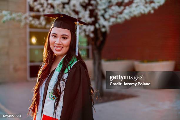 ritratto ravvicinato di un'allegra giovane donna ispanica che indossa un berretto e un abito in primavera prima della laurea. la sua fascia mostra una bandiera messicana per rappresentare con orgoglio il suo viaggio e il patrimonio familiare - fusciacca foto e immagini stock