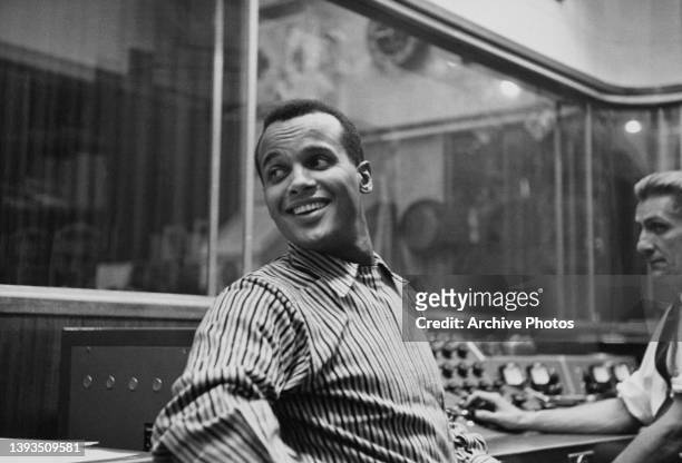 American singer-songwriter and civil rights activist Harry Belafonte, wearing a striped shirt, in an recording studio, circa 1957. The sound engineer...