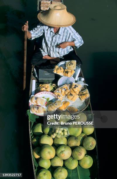 Un homme en vue plongeante dans sa barque de fruits au marché flottant de Damnoen Saduak en Thaïlande, années 1990.