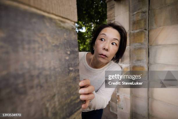 mujer asustada mirando a la vuelta de una esquina - mirar alrededor fotografías e imágenes de stock