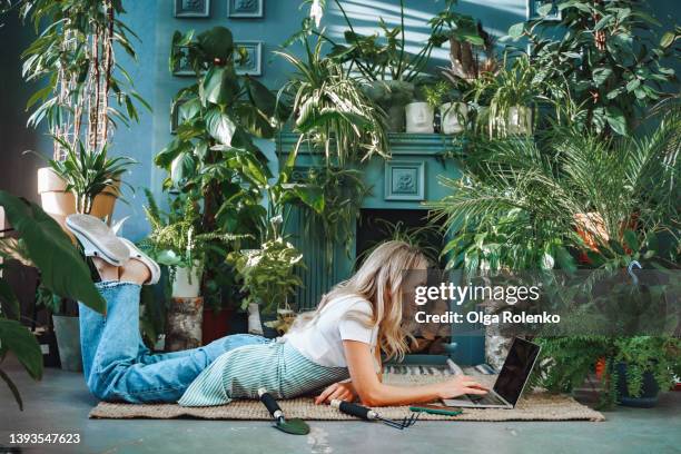 confident and professional blond businesswoman lying on the floor, working online on laptop and typing in smartphone at flower market. - ligga på mage bildbanksfoton och bilder