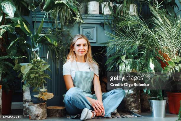 portrait of a cheerful and calm smiling young woman in a small gardening shop siting with legs across - reconversão profissional imagens e fotografias de stock