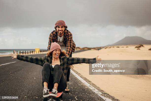 paar hat spaß mit skateboard auf der straße in der nähe des meeres - hipster adventure stock-fotos und bilder