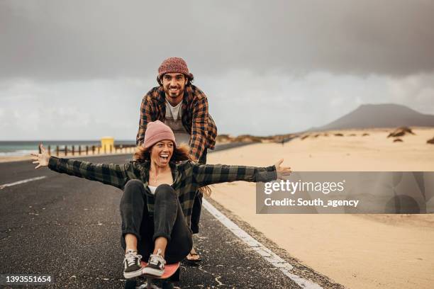 pareja divirtiéndose con el monopatín en la carretera cerca del mar - amor y amistad fotografías e imágenes de stock