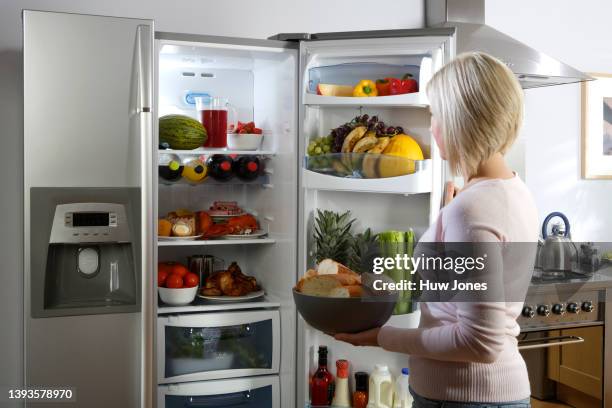 a young woman looking in an open fridge filled with food and drinks in a home kitchen - feeling full stock pictures, royalty-free photos & images