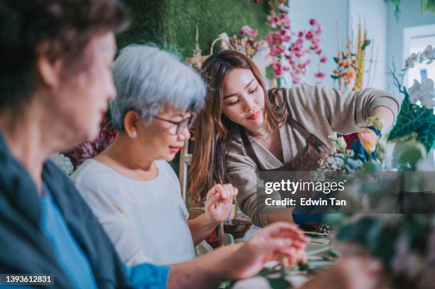 asian chinese senior women learning flower arrangement from female florist at flower shop - craft table stock pictures, royalty-free photos & images