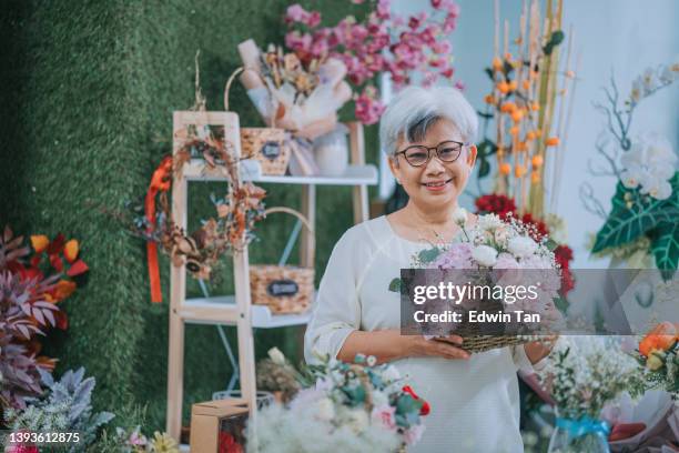 proud asian chinese senior women holding her own flower basket creation looking at camera smiling in the flower shop after her flower arrangement class - craft show stock pictures, royalty-free photos & images