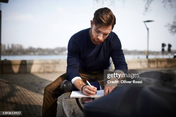 young man sitting on a bench taking notes - bank student stock-fotos und bilder
