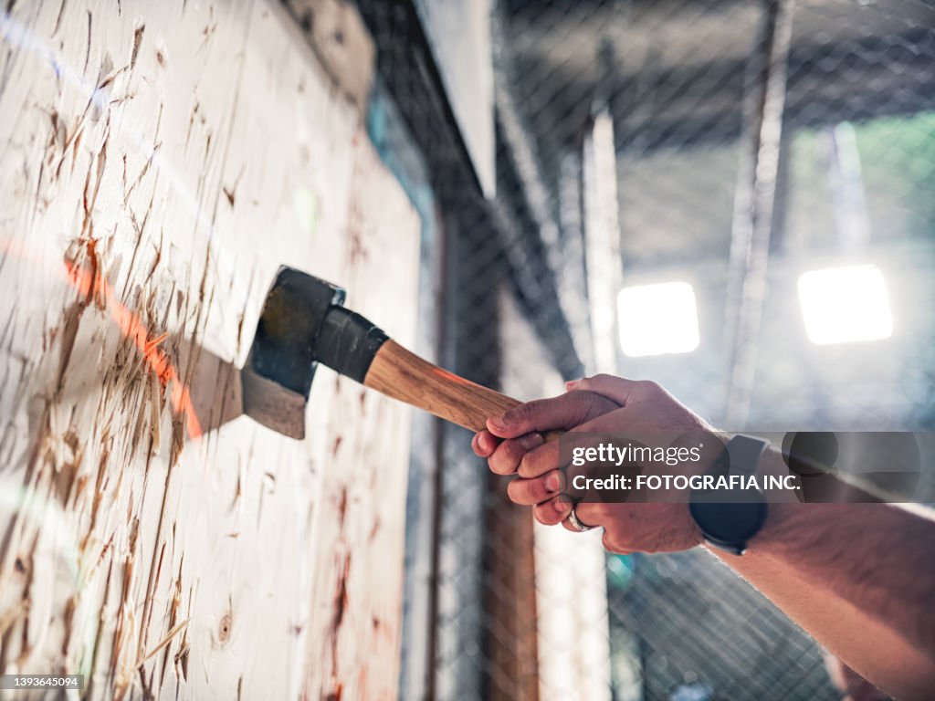 Young gay man throwing axe at the game range