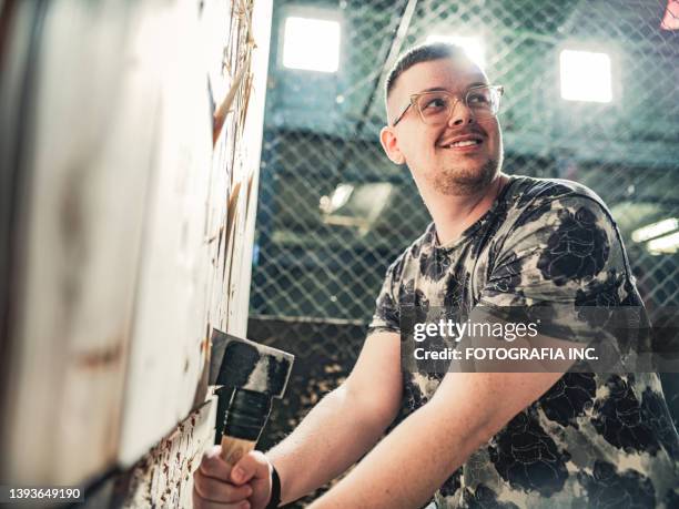 young gay man throwing axe at the game range - axe throwing stock pictures, royalty-free photos & images