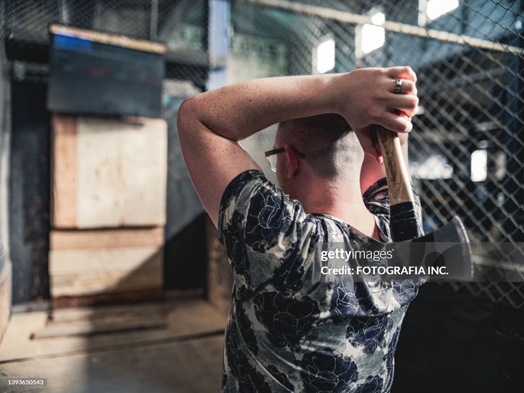 Young gay man throwing axe at the game range