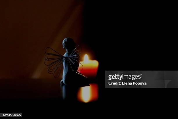 angel wings silhouette against wax burning candle - mourning candles stock pictures, royalty-free photos & images